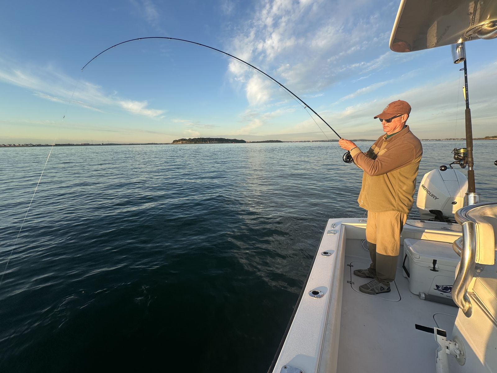 Angler fighting a striped bass at sunset with the Boston skyline behind